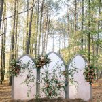 White three-panel gothic arch ceremony backdrop decorated with orange roses and greenery in forest setting