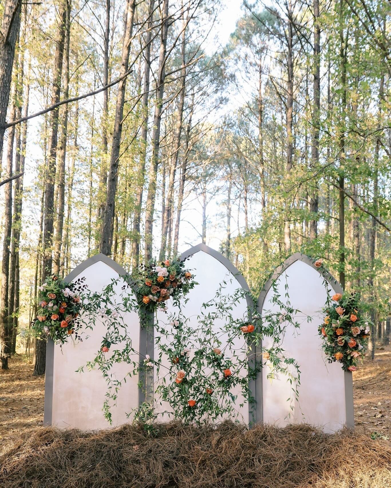 White three-panel gothic arch ceremony backdrop decorated with orange roses and greenery in forest setting