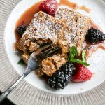 French toast dusted with powdered sugar, accompanied by fresh berries and mint on white plate