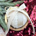 Custom wedding dress keepsake ornament with lace fabric and ribbon on wood base surrounded by pink sequins and greenery