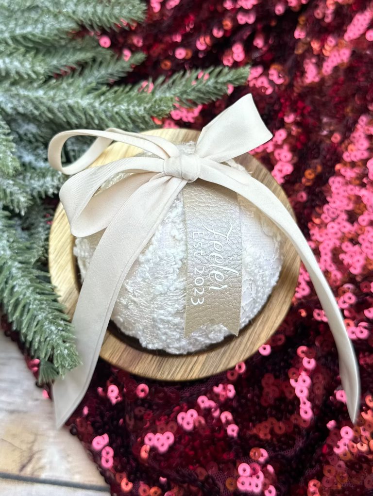 Custom wedding dress keepsake ornament with lace fabric and ribbon on wood base surrounded by pink sequins and greenery