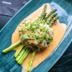 Grilled asparagus spears topped with creamy sauce on blue ceramic plate