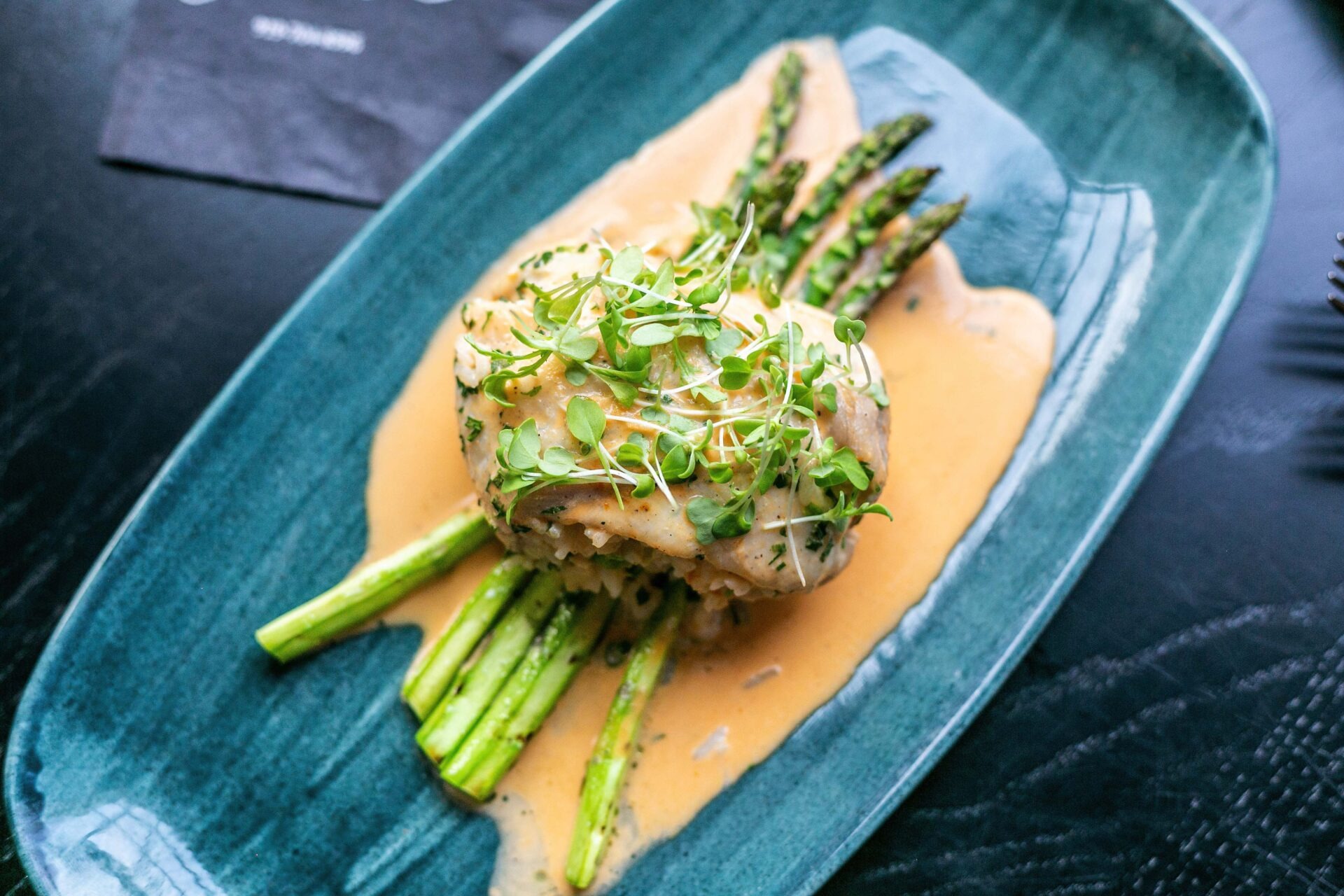 Grilled asparagus spears topped with creamy sauce on blue ceramic plate