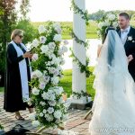 Bride and groom exchanging vows at outdoor waterfront ceremony with floral arch