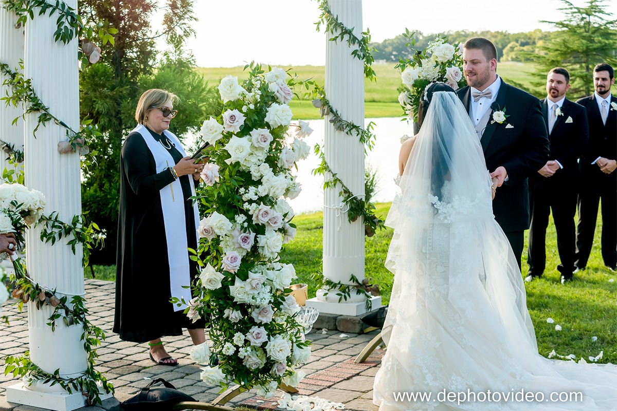 Bride and groom exchanging vows at outdoor waterfront ceremony with floral arch