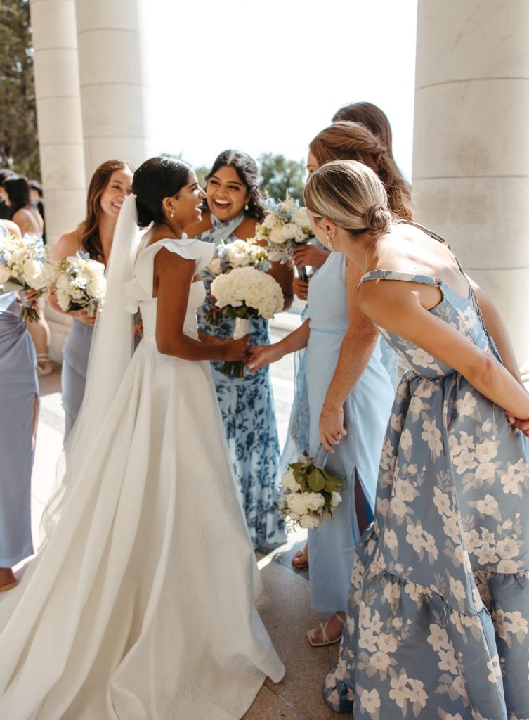 Bride surrounded by wedding party holding white floral bouquets between white columns