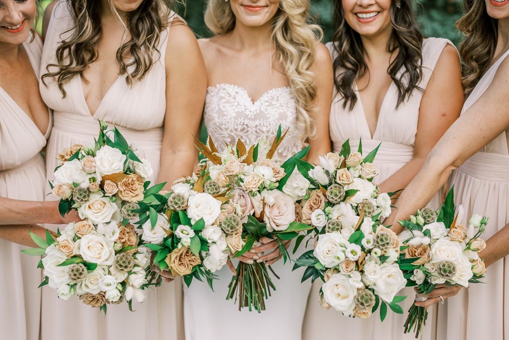 Bridesmaids in neutral gowns holding white and green wedding bouquets