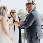 Reverend Susie officiating an outdoor wedding ceremony with couple exchanging rings under floral arch