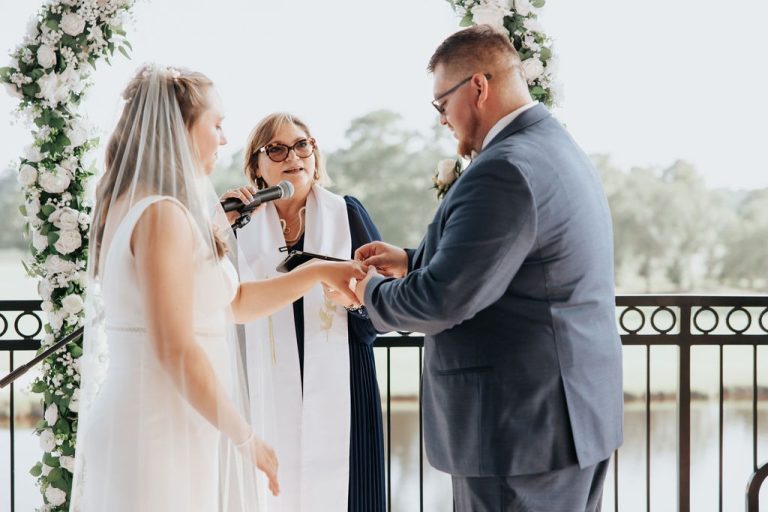 Reverend Susie officiating an outdoor wedding ceremony with couple exchanging rings under floral arch