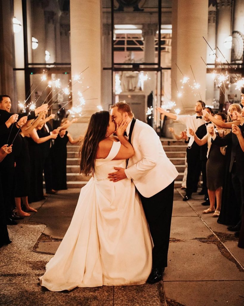 Bride and groom kissing in front of rows of guests with sparklers. Captured by Blue Willow Photo & Video.