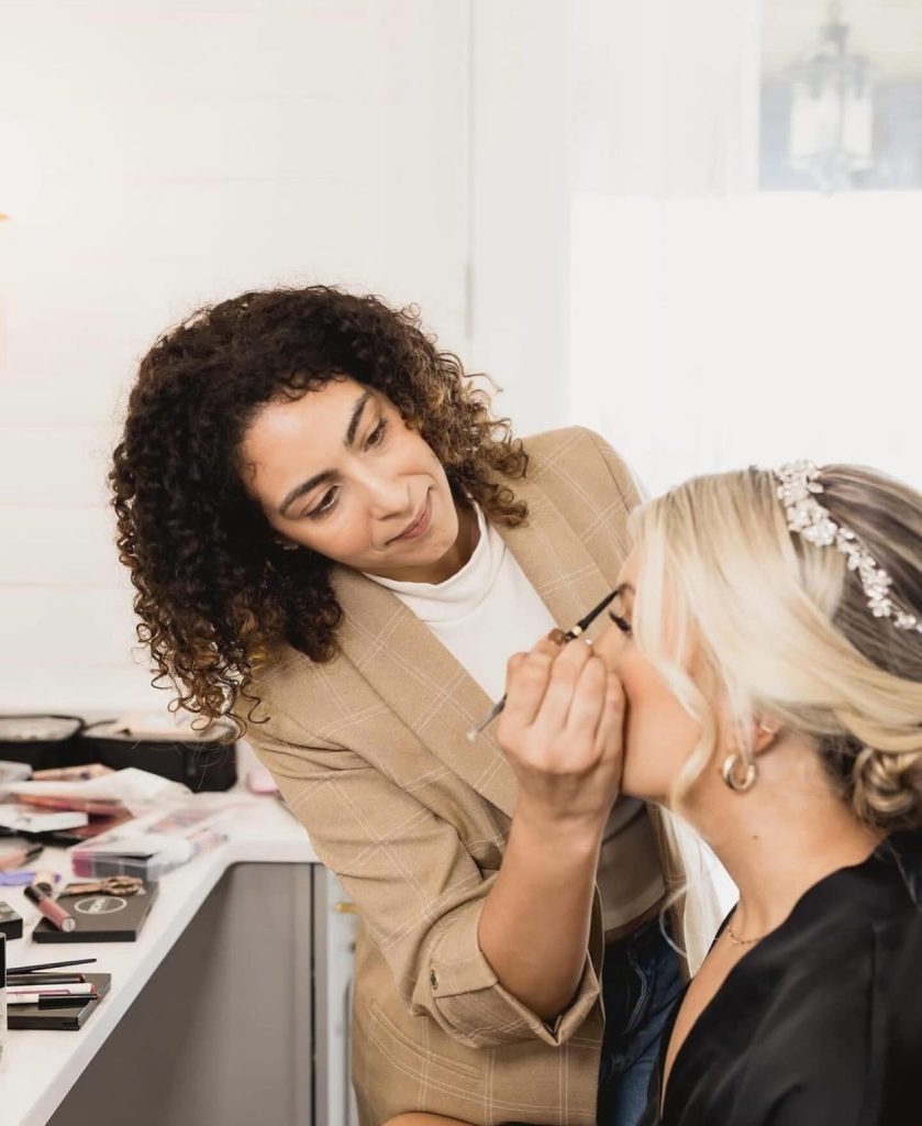 Makeup artist applying bride's makeup with brush in professional salon