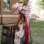 Romantic wedding bouquet with blush roses, trailing amaranthus, and bridal heels displayed on weathered barrel outdoors