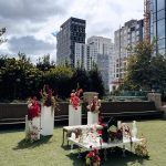 Persian Sofreh Aghd wedding spread with white ceremonial table, pink and burgundy floral arrangements on pillars, and urban rooftop backdrop