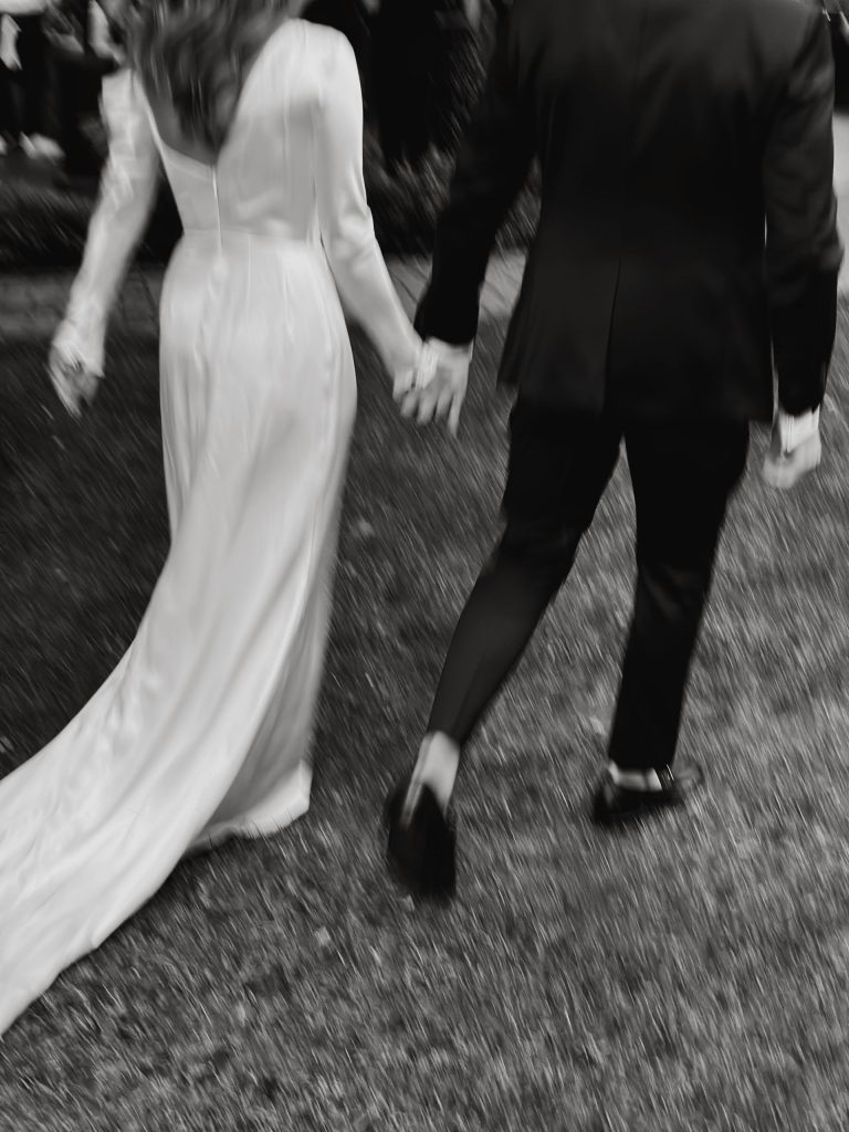 Motion-blurred black and white photo of bride and groom walking together, capturing wedding day moments