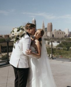 Couple in formal wedding attire embraces on rooftop with Cleveland downtown buildings visible