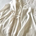 Ivory silk wedding gown with delicate lace detailing and flowing fabric draped on white bedding