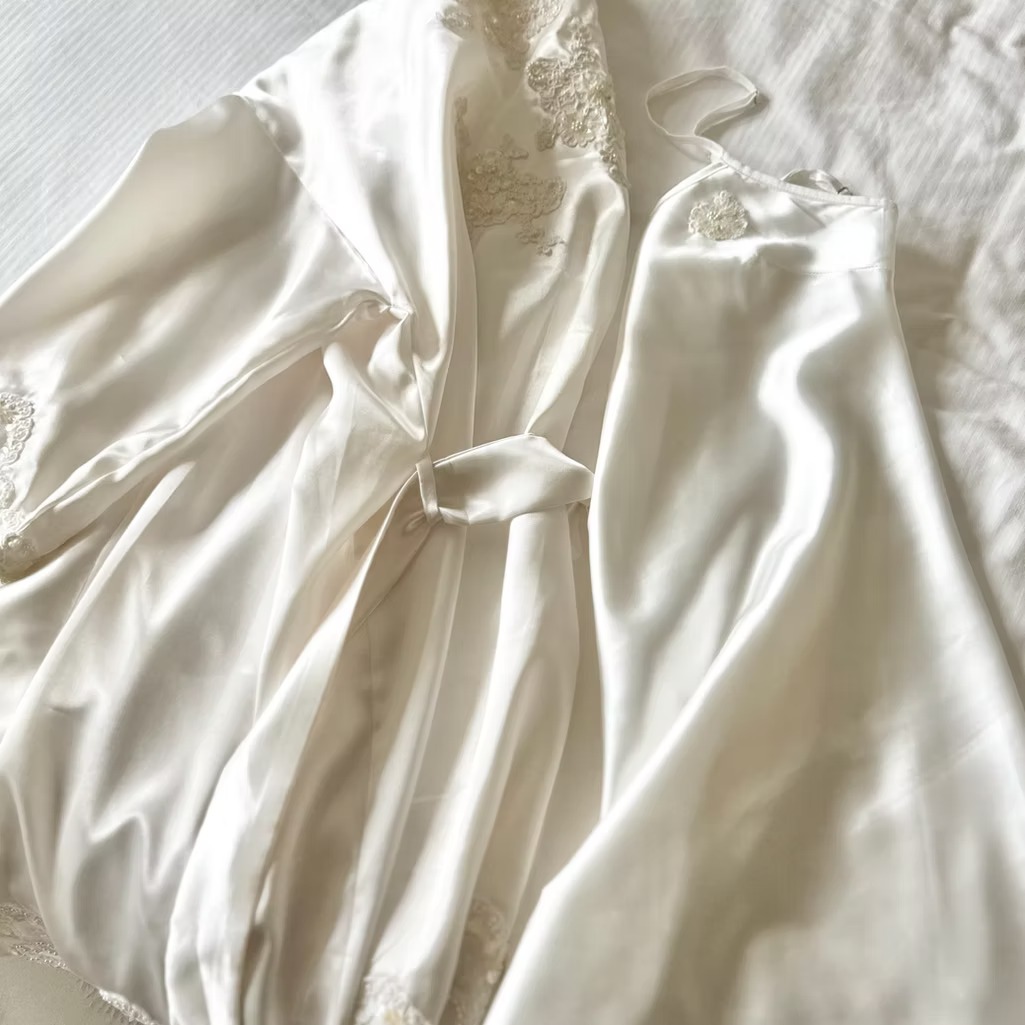 Ivory silk wedding gown with delicate lace detailing and flowing fabric draped on white bedding