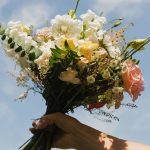 Hand holding wedding bouquet with white poppies, pink roses, and eucalyptus against blue sky