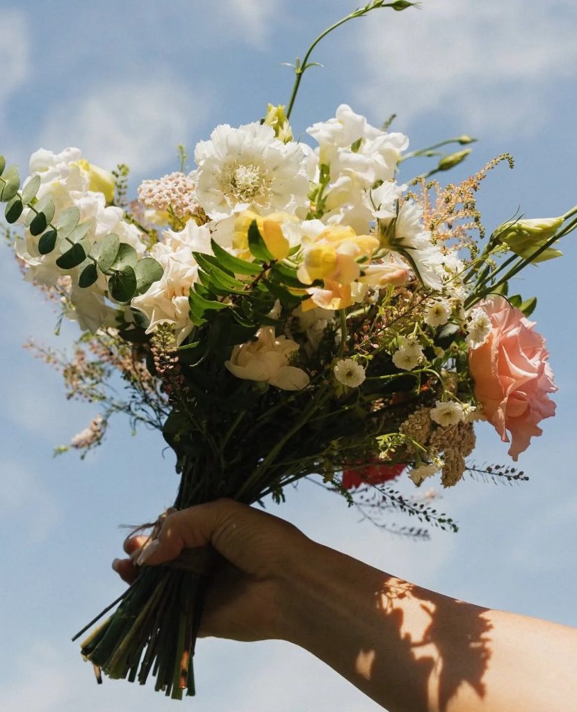 Hand holding wedding bouquet with white poppies, pink roses, and eucalyptus against blue sky