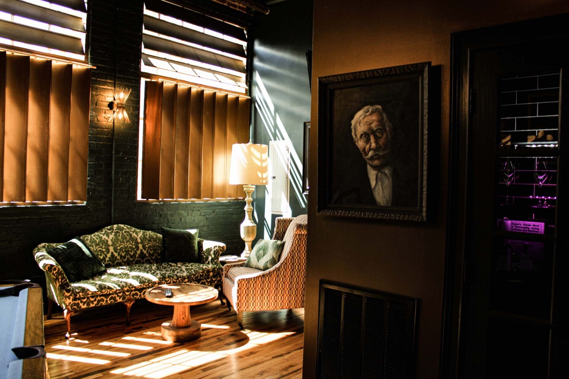 Elegant lounge with vintage seating, backlit shutters, and classical portrait creating intimate rehearsal dinner ambiance