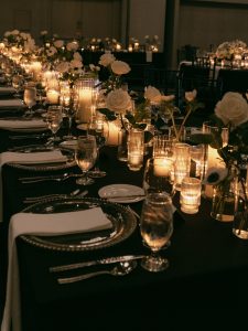 Elegant wedding reception table with black linens, white roses, and glowing candles creating romantic ambiance