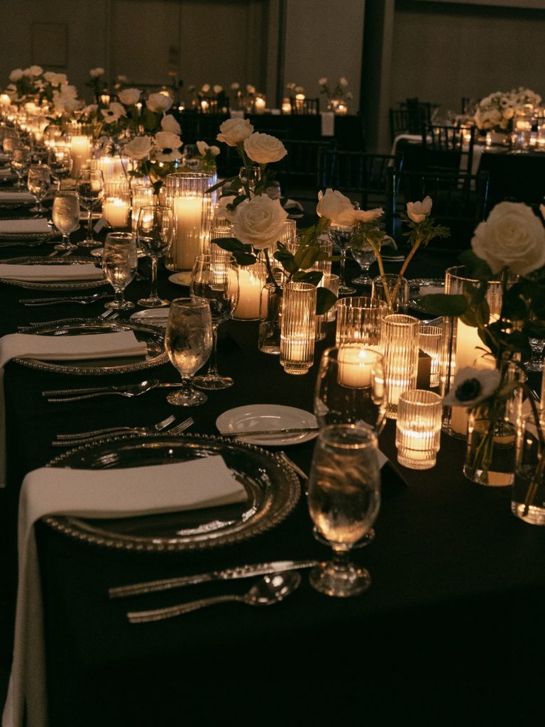 Elegant wedding reception table with black linens, white roses, and glowing candles creating romantic ambiance