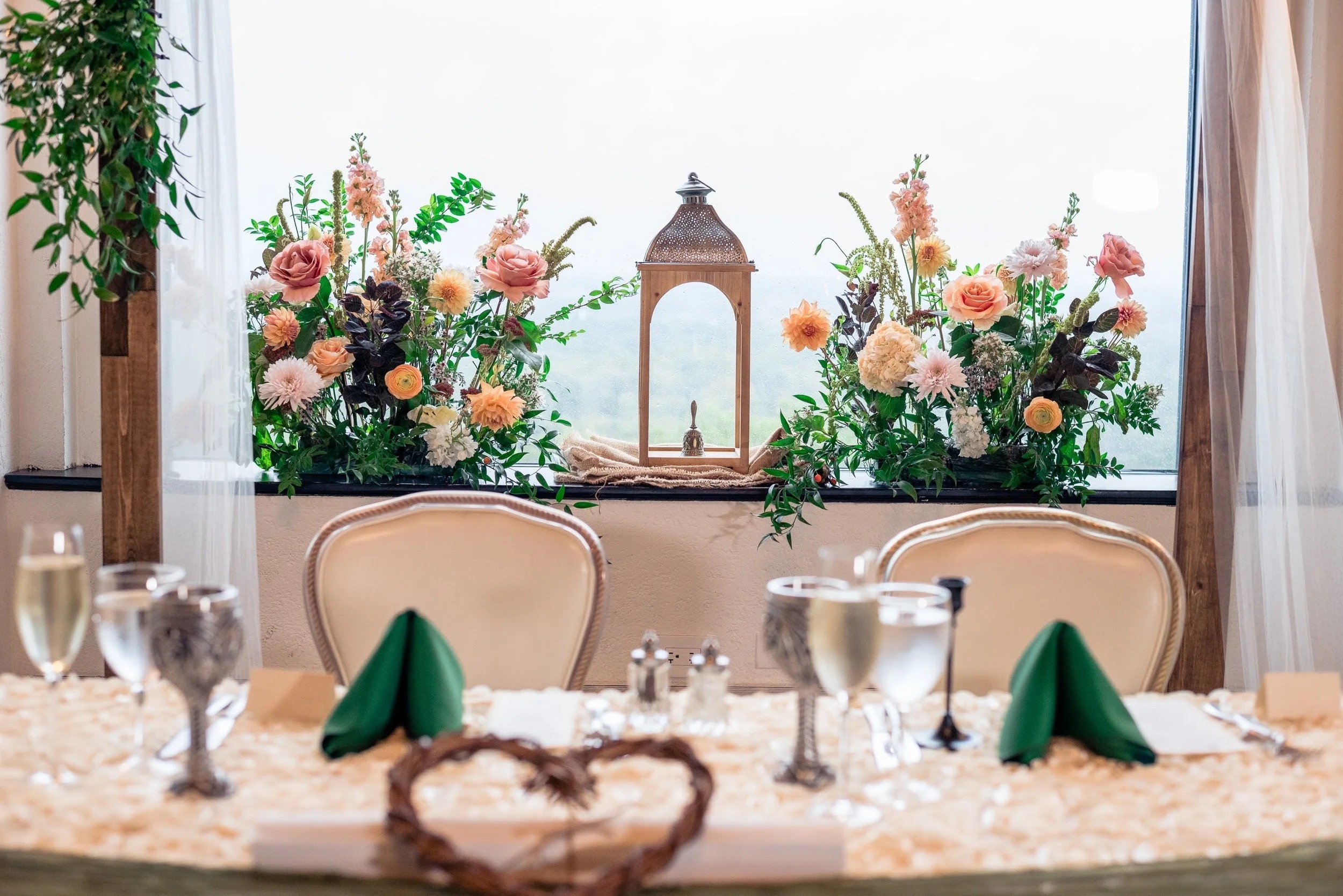 Rustic wedding reception tablescape with coral and peach floral centerpieces flanking copper lantern