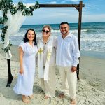 Wedding officiant with couple at beachfront ceremony under natural arbor