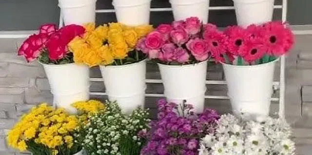 Bloom bar display with fresh flowers in white buckets arranged in tiers, featuring roses, gerberas, and mums