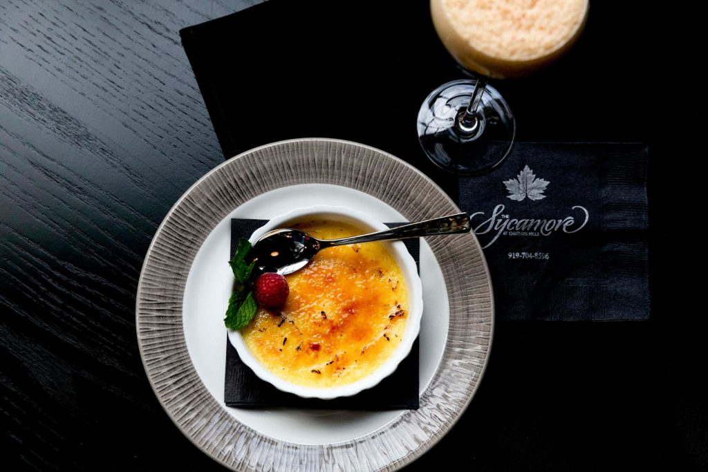 Elegant crème brûlée dessert with caramelized top, garnished with raspberry and mint, served at Sycamore at Carters Mill
