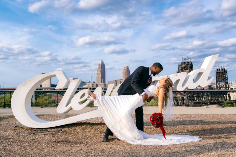 Groom dipping bride with flowing white wedding dress against Cleveland skyline
