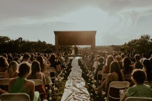 Outdoor wedding ceremony at sunset with guests seated along aisle leading to modern architectural structure