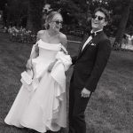 Smiling bride and groom wearing sunglasses in garden setting, black and white photograph