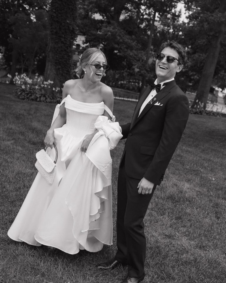 Smiling bride and groom wearing sunglasses in garden setting, black and white photograph