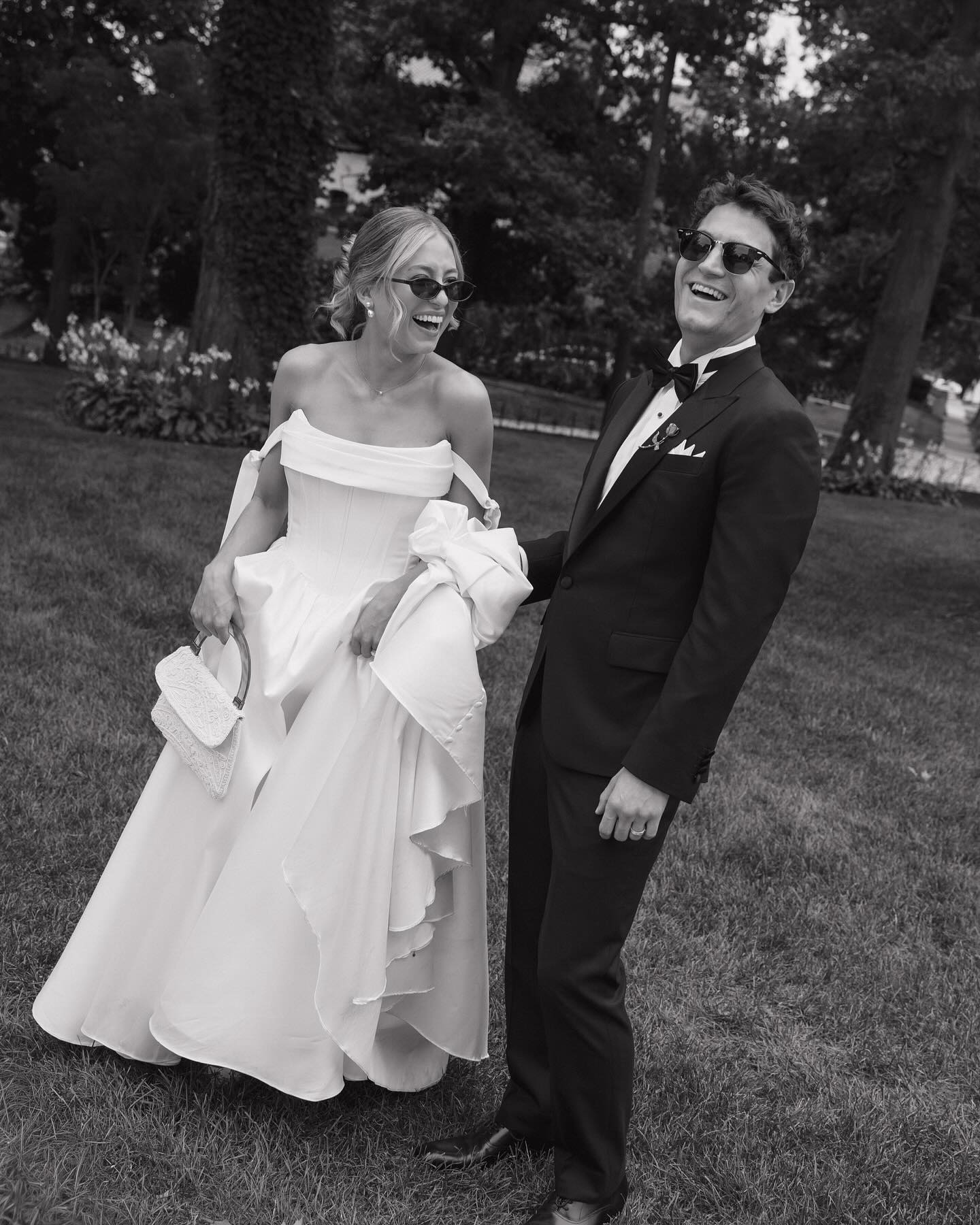 Smiling bride and groom wearing sunglasses in garden setting, black and white photograph