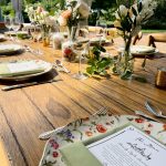 Rustic wooden farm table set with elegant greenery centerpieces and place settings for outdoor wedding reception