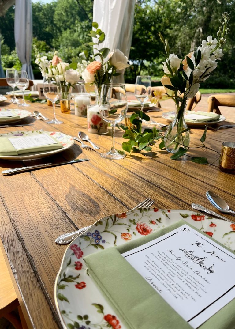 Rustic wooden farm table set with elegant greenery centerpieces and place settings for outdoor wedding reception