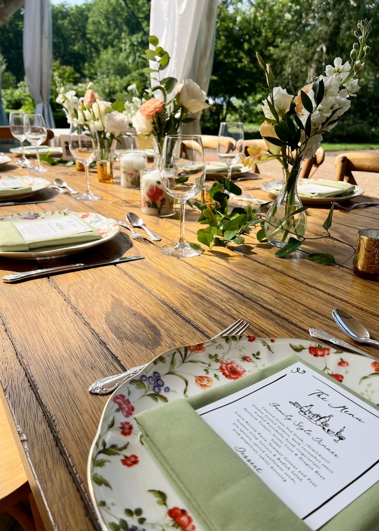 Rustic wooden farm table set with elegant greenery centerpieces and place settings for outdoor wedding reception