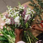 Florist binding stems of white and purple wedding flowers with pink tulips and eucalyptus beside red pruning shears