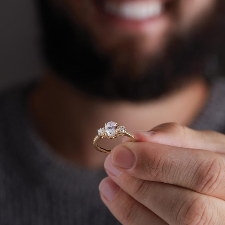 Hand holding delicate diamond engagement ring against blurred background