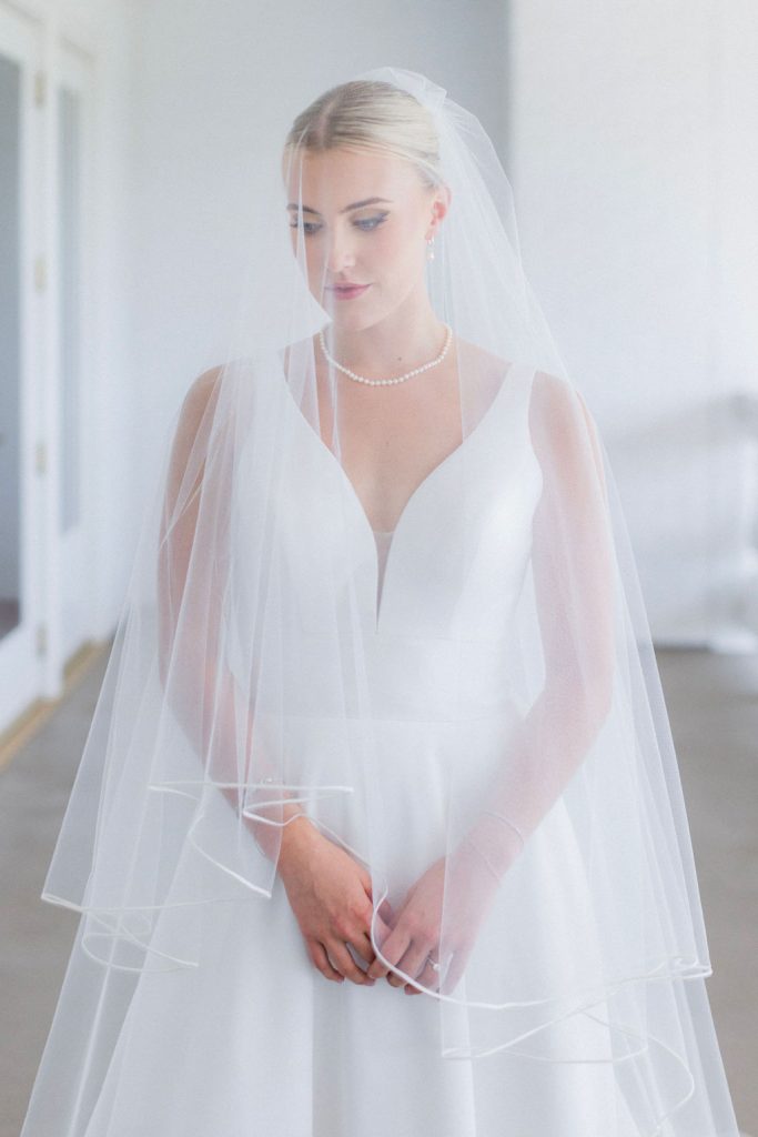 Bride Catherine in minimalist V-neck gown wearing tiered veil and pearl necklace in natural light