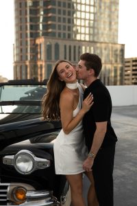 Haley and Todd posing with classic car on urban rooftop during engagement session