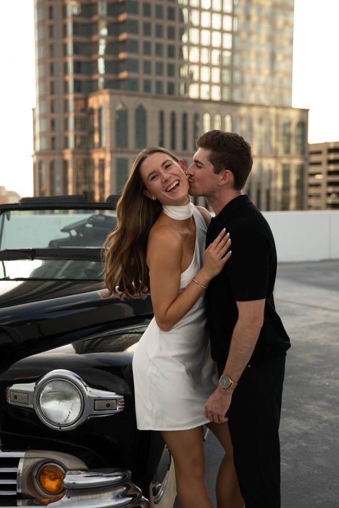 Haley and Todd posing with classic car on urban rooftop during engagement session
