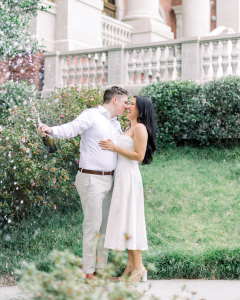 Couple during engagement photo shoot popping a bottle of champange while kissing.
