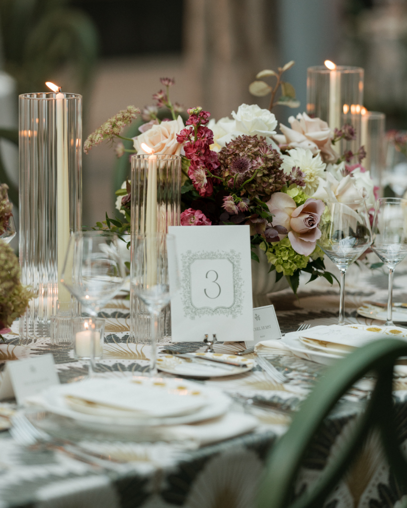 Reception table detail with floral centerpiece, candles, elegant place settings, and table number display