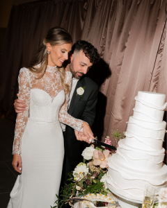 Bride and groom Cathy and Charlie cutting a multi-tier white wedding cake in an intimate, candlelit reception setting