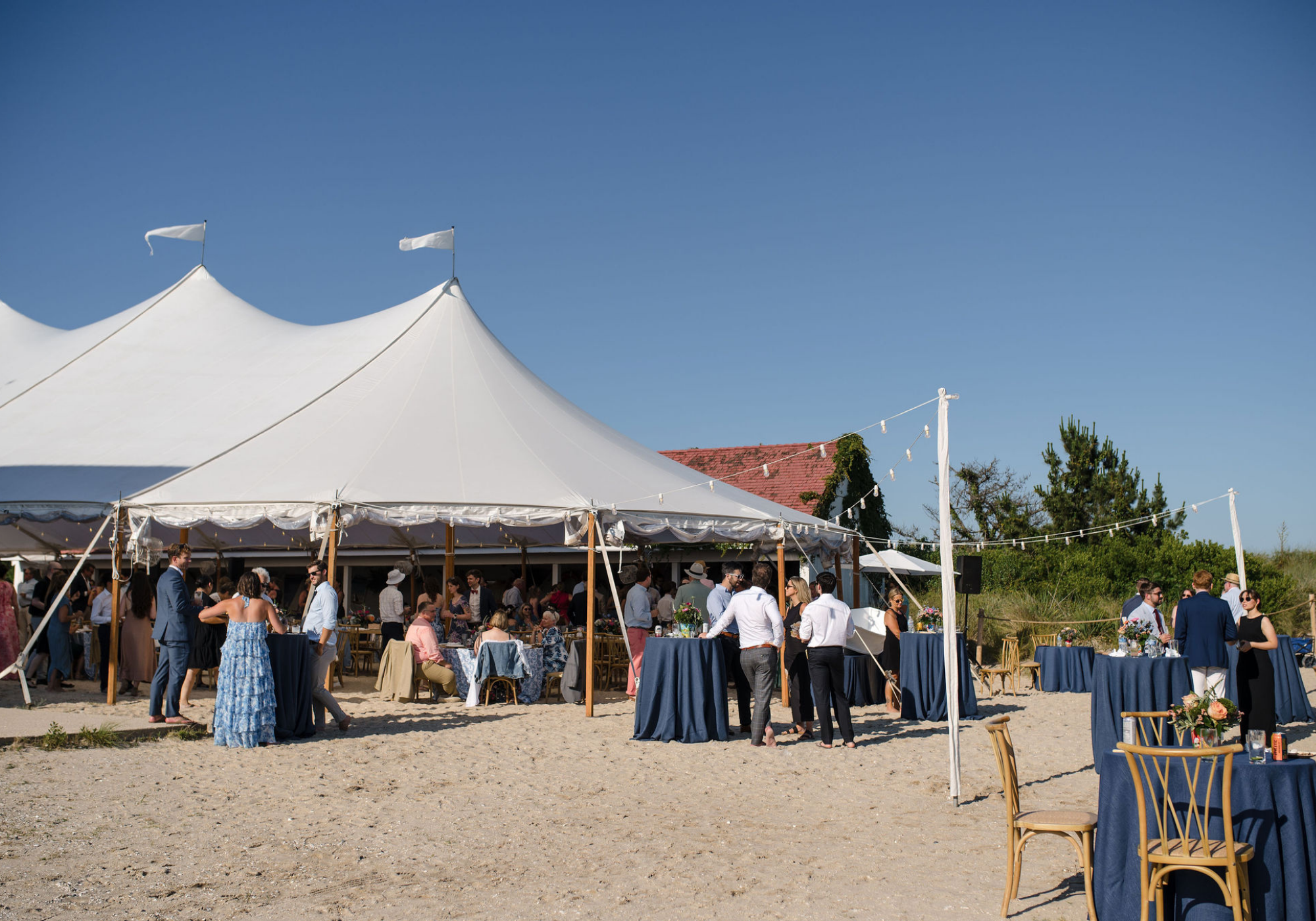 Guests gather outside a sailcloth tent on the Delaware beach before the waterfront wedding ceremony.