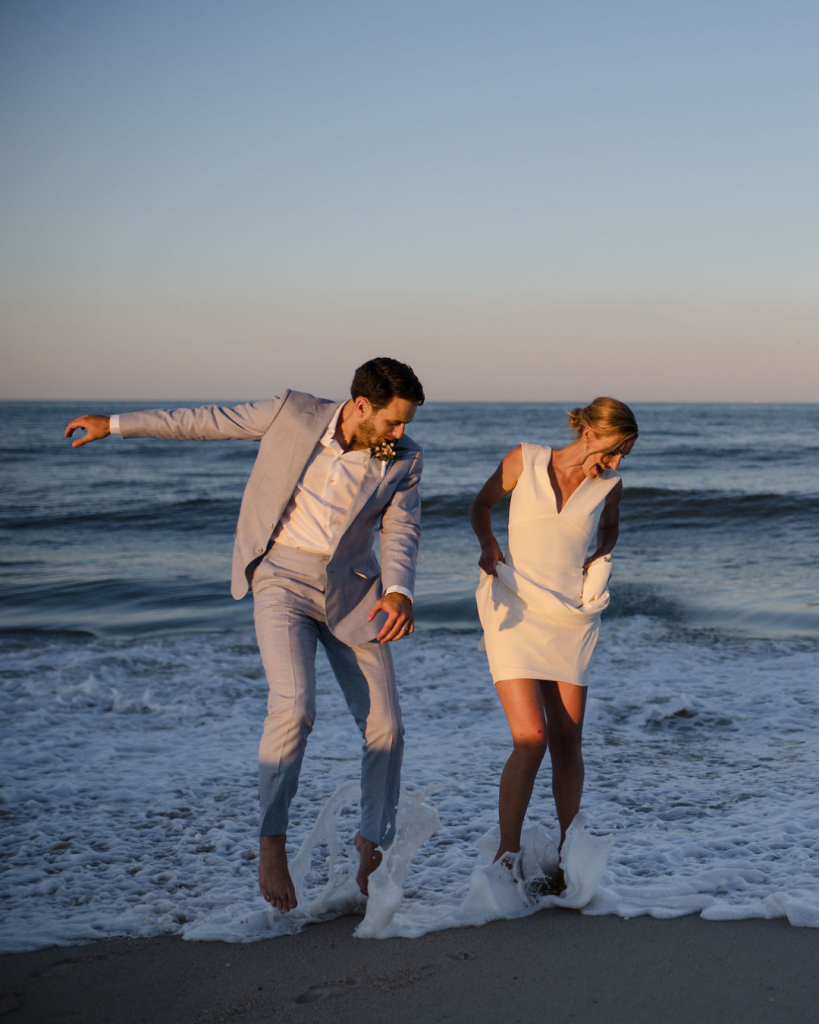 Bride and groom walk barefoot along the beach at sunset on the Delaware coast before their waterfront wedding.