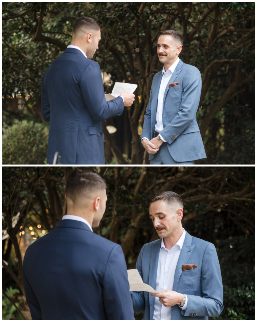 Two grooms exchange vows during an intimate outdoor ceremony beneath trees while standing face to face.