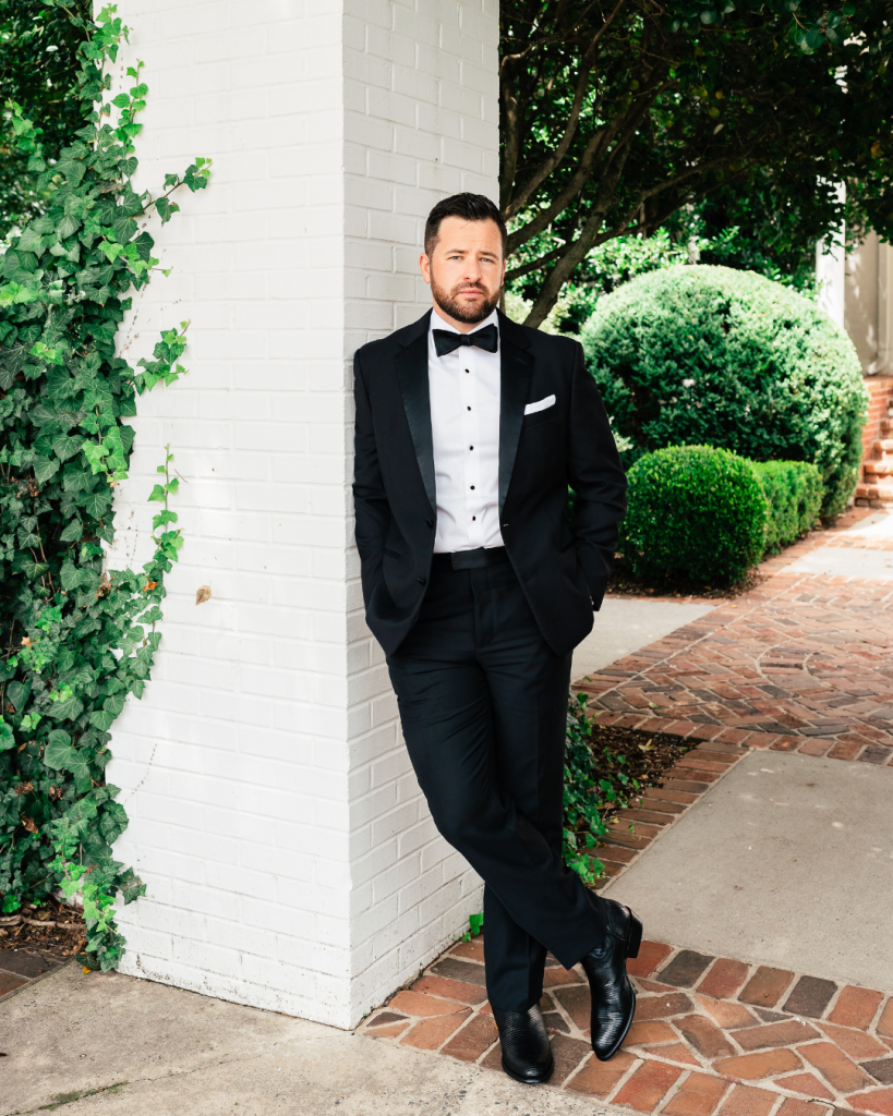 Groom Addison in a classic black tuxedo standing outside Quail Hollow Clubhouse before the wedding ceremony in Charlotte
